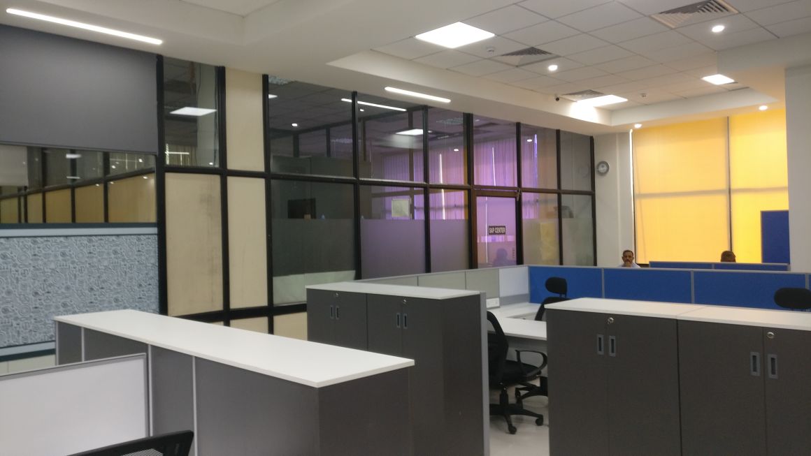 Wide-angle view of Minda Industries open-plan floor with grey storage units, blue workstation panels and glass meeting rooms